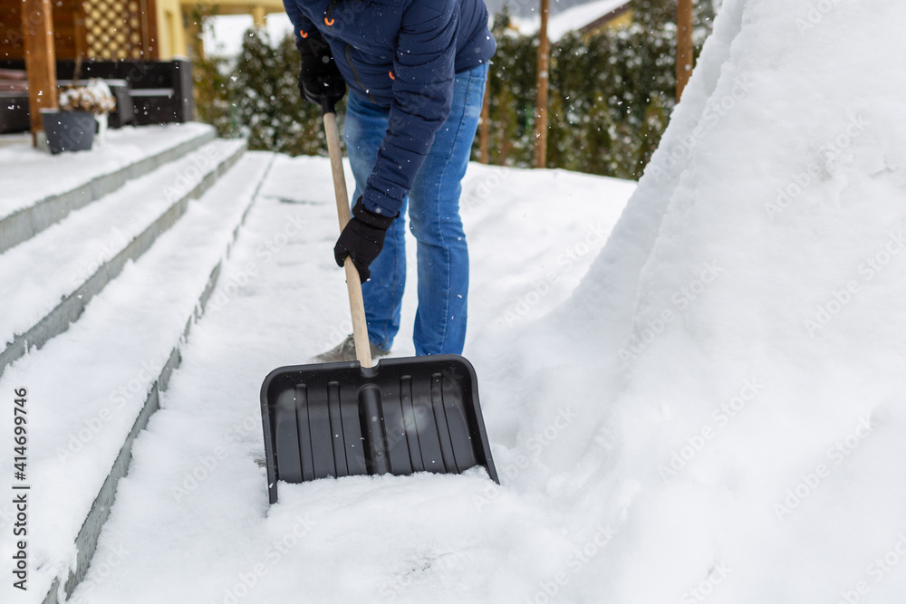 用铲子清除房子前面车道的积雪