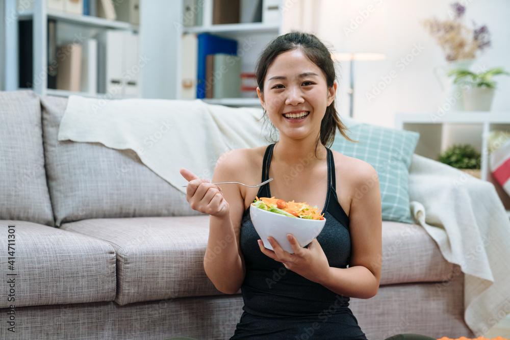 年轻的亚洲优雅女人在家锻炼后吃着一碗健康沙拉。快乐的女孩脸ca