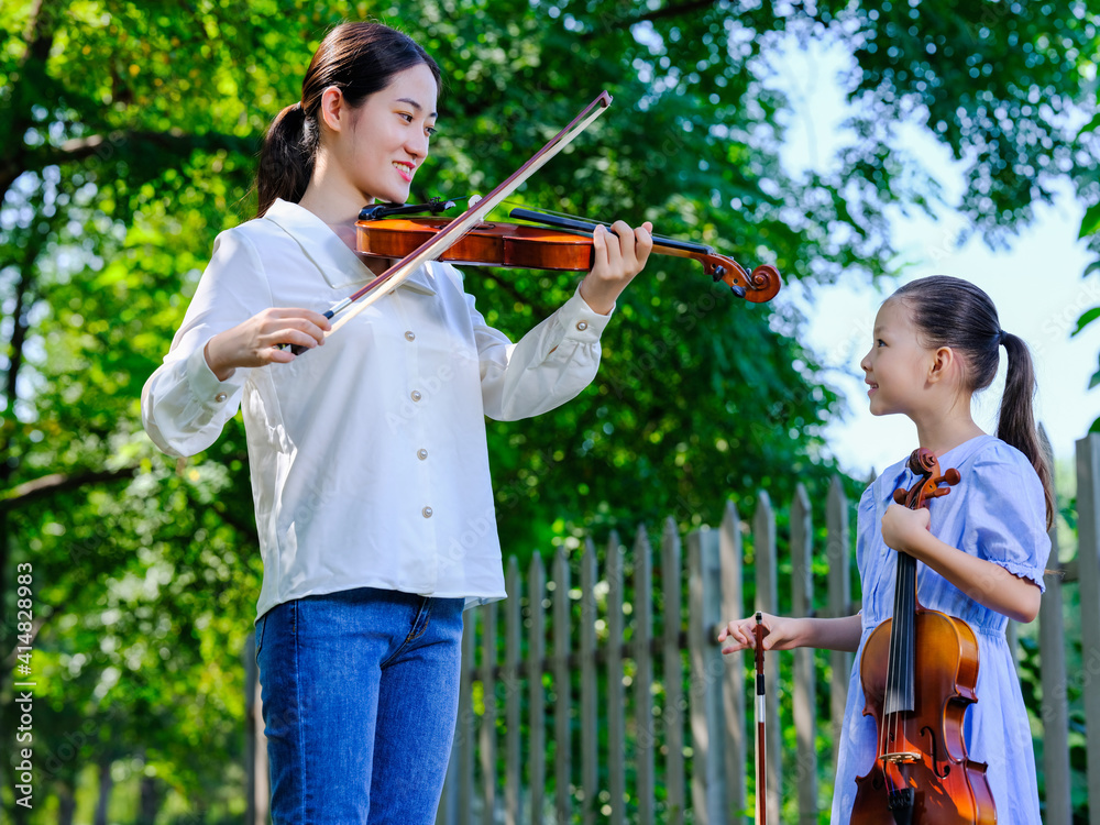 Young women instruct girls to play the violin in the park