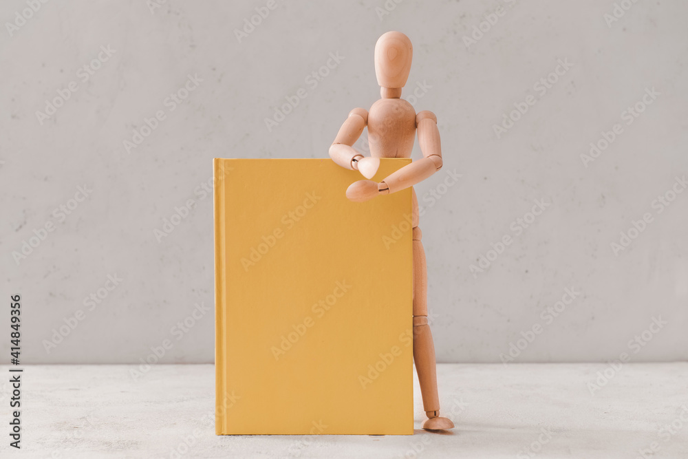 Wooden mannequin with book on light background