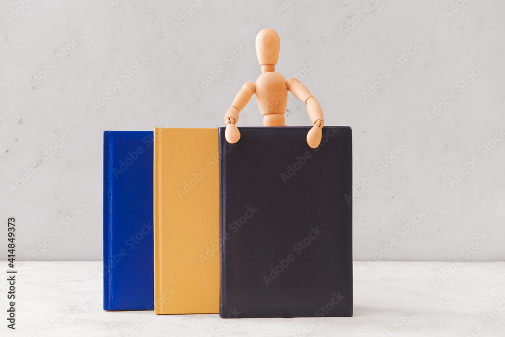 Wooden mannequin with books on light background