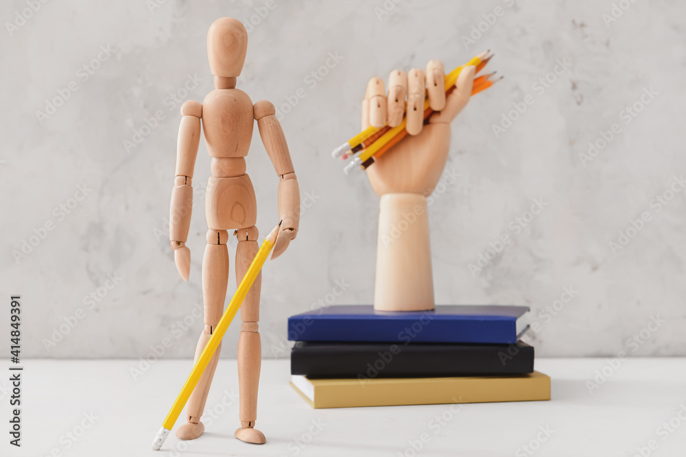 Wooden mannequin with books and pencils on light background