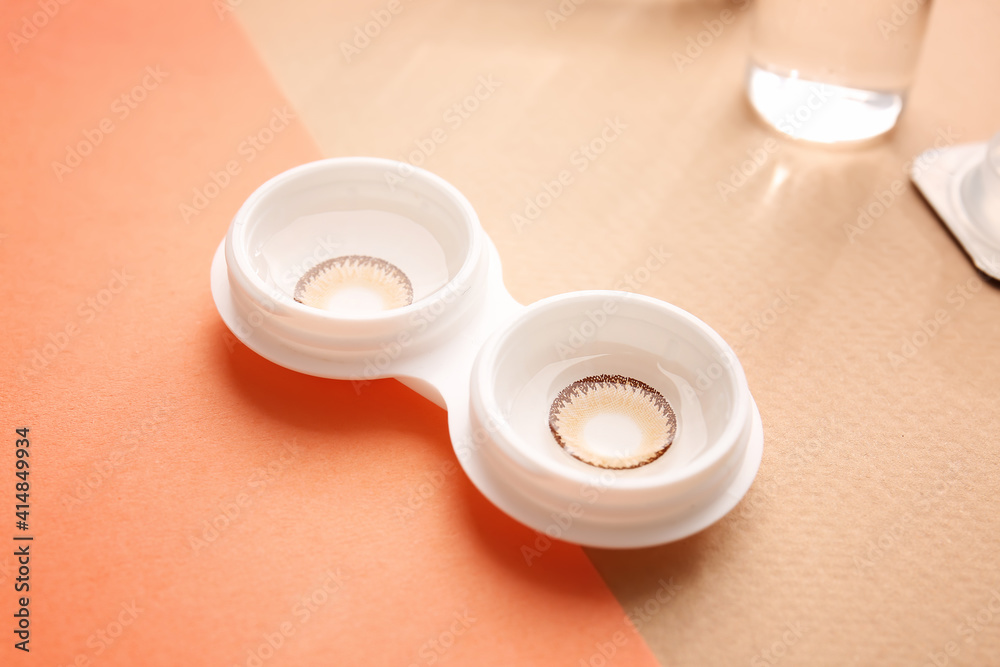 Container with contact lenses on color background