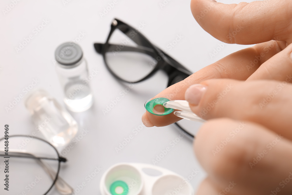 Female hands with tweezers and contact lens on light background