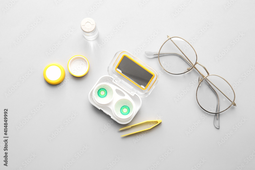 Eyeglasses, tweezers and container with contact lenses on light background