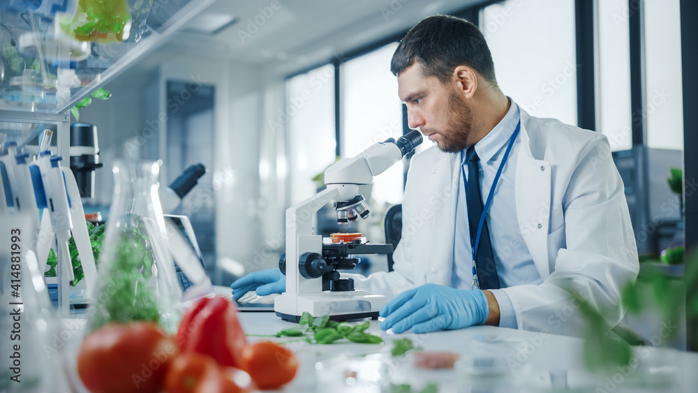 戴着安全眼镜的英俊男科学家通过高级麦克风分析实验室培育的食品样本