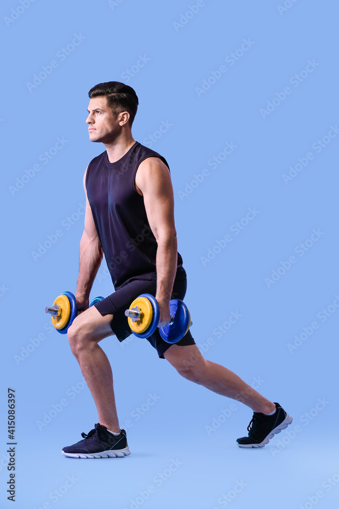 Sporty young man training with dumbbells on color background