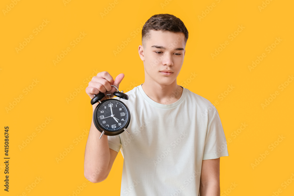 Teenager with alarm clock on color background