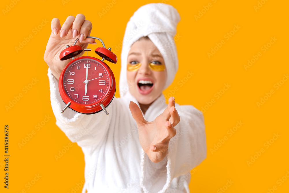 Stressed young woman with alarm clock on color background