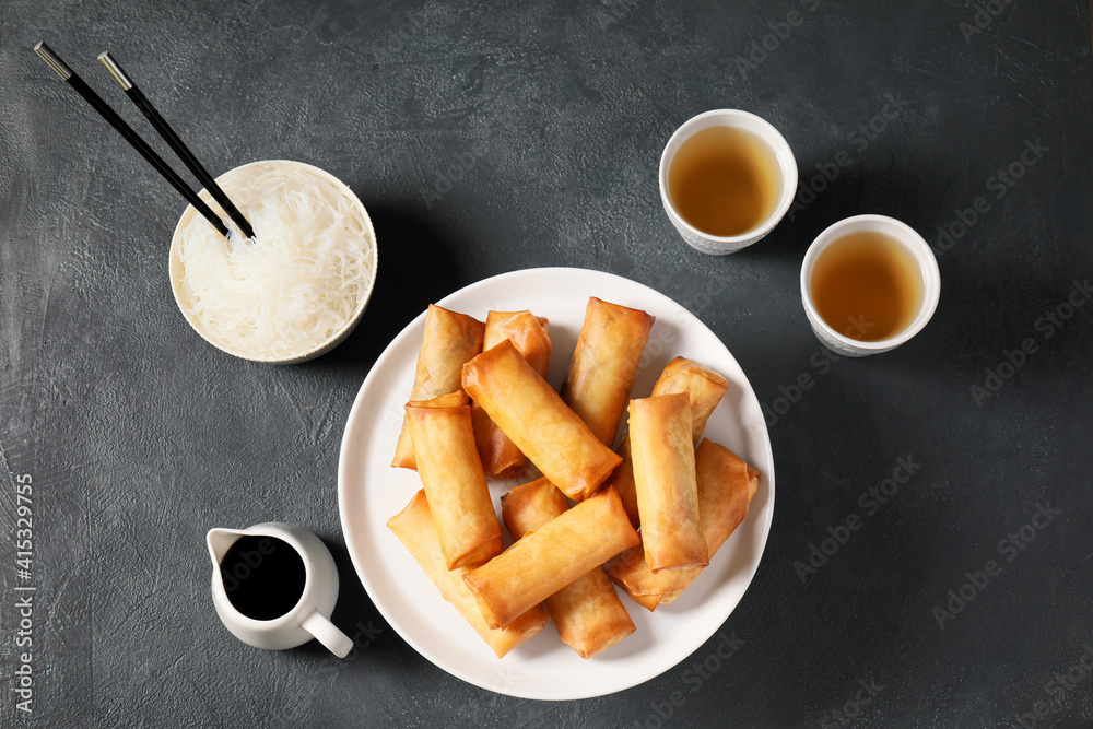 Stand with tasty fried spring rolls and sauce on dark background