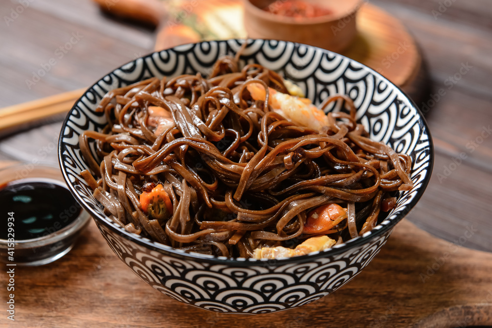 Bowl with tasty soba noodles and seafood on wooden background