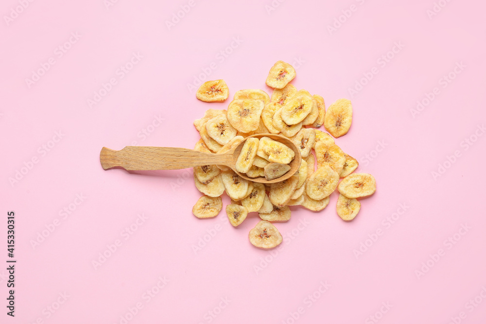 Wooden spoons with crispy banana chips on color background