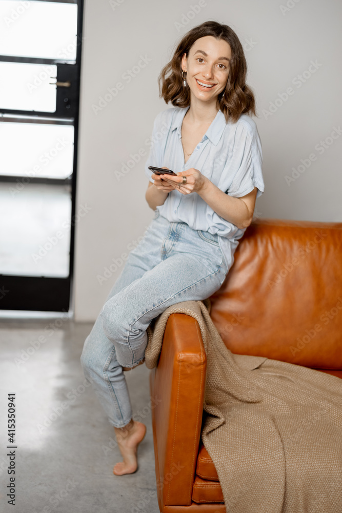 Beautiful woman using Smartphone while sitting on sofa in stylish design interior of living room. Lo