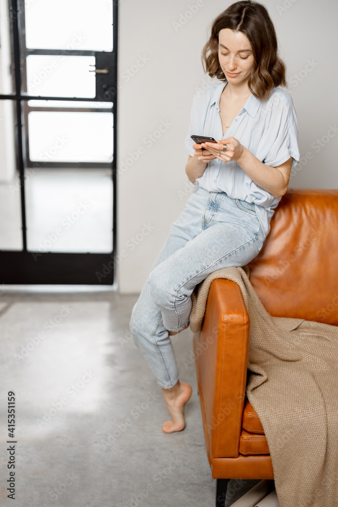 Beautiful woman using Smartphone while sitting on sofa in stylish design interior of living room. Hi