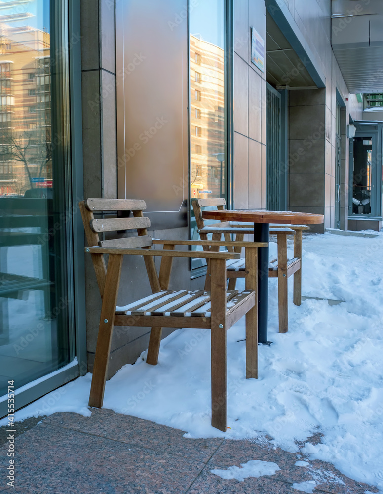 Table and chairs of a street cafe in winter is covered with snow.