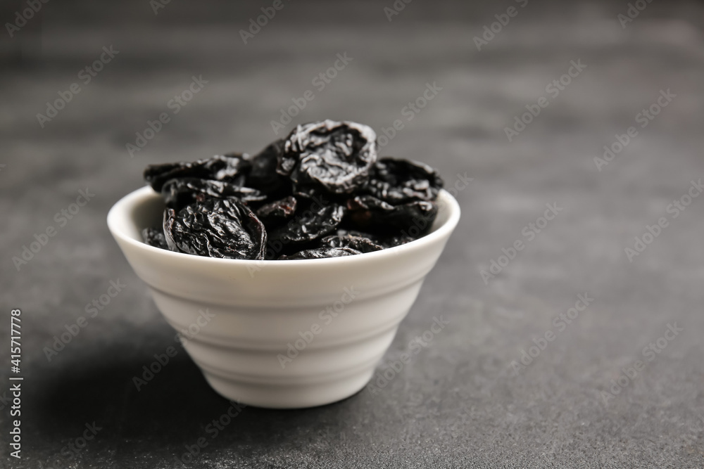 Bowl with dried prunes on dark background