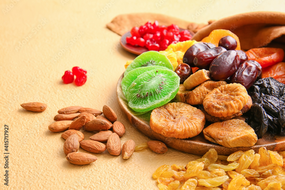 Plate with different dried fruits and nuts on color background