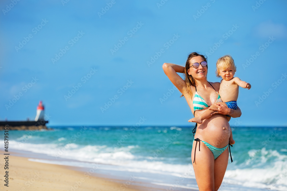 Happy laughing portrait of a mother hold little blond smiling toddler pointing with finger boy on th