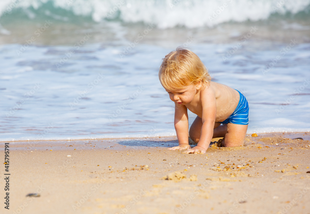 Little blond toddler boy crawl on the sand beach near sea waves