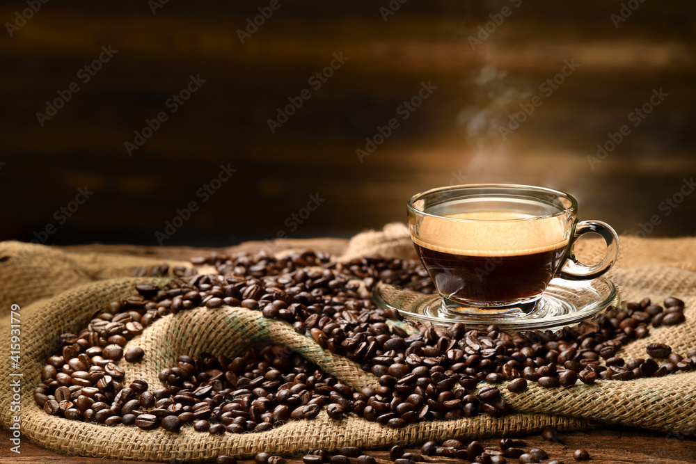 Cup glass of coffee with smoke and coffee beans on burlap sack on old wooden background