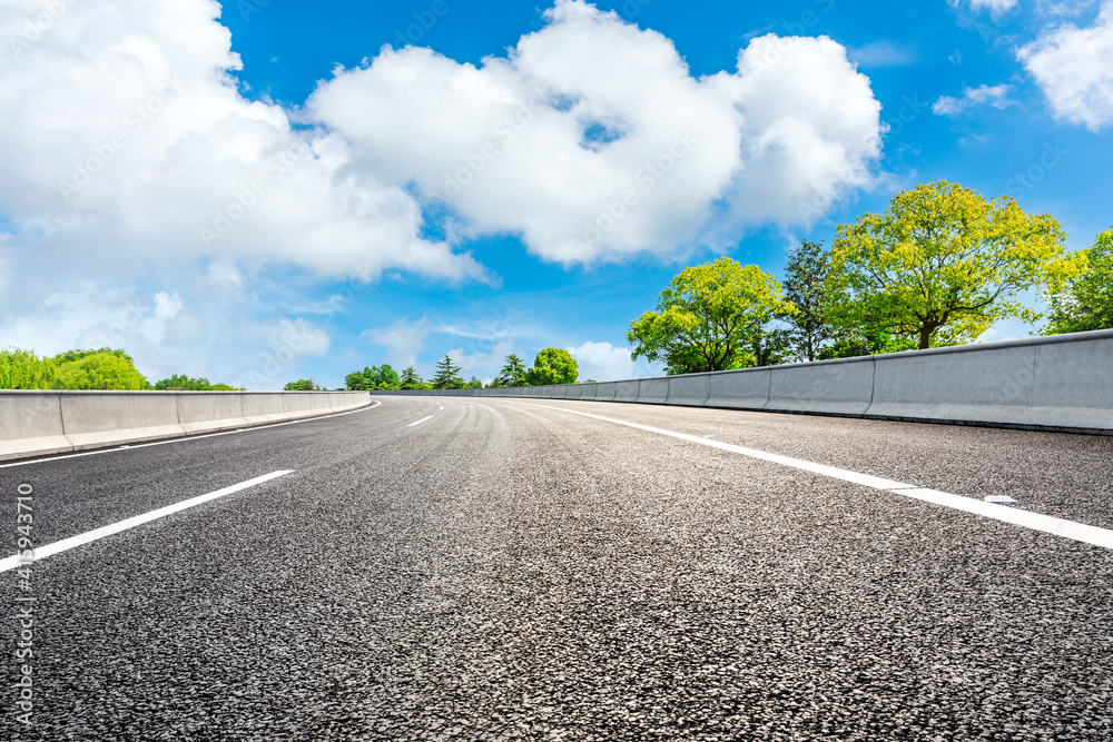 空旷的道路和蓝天下的绿树。