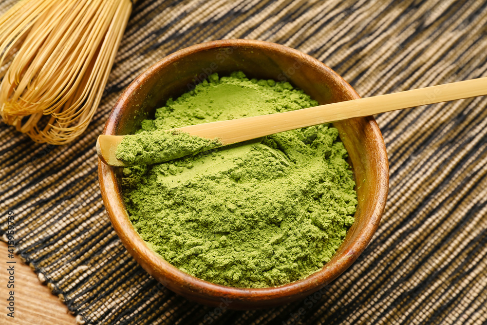 Bowl with powdered matcha tea, chashaku and chasen on wooden background, closeup