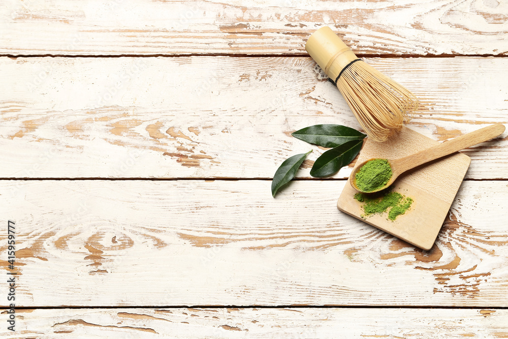 Spoon with powdered matcha tea and chasen on light wooden background