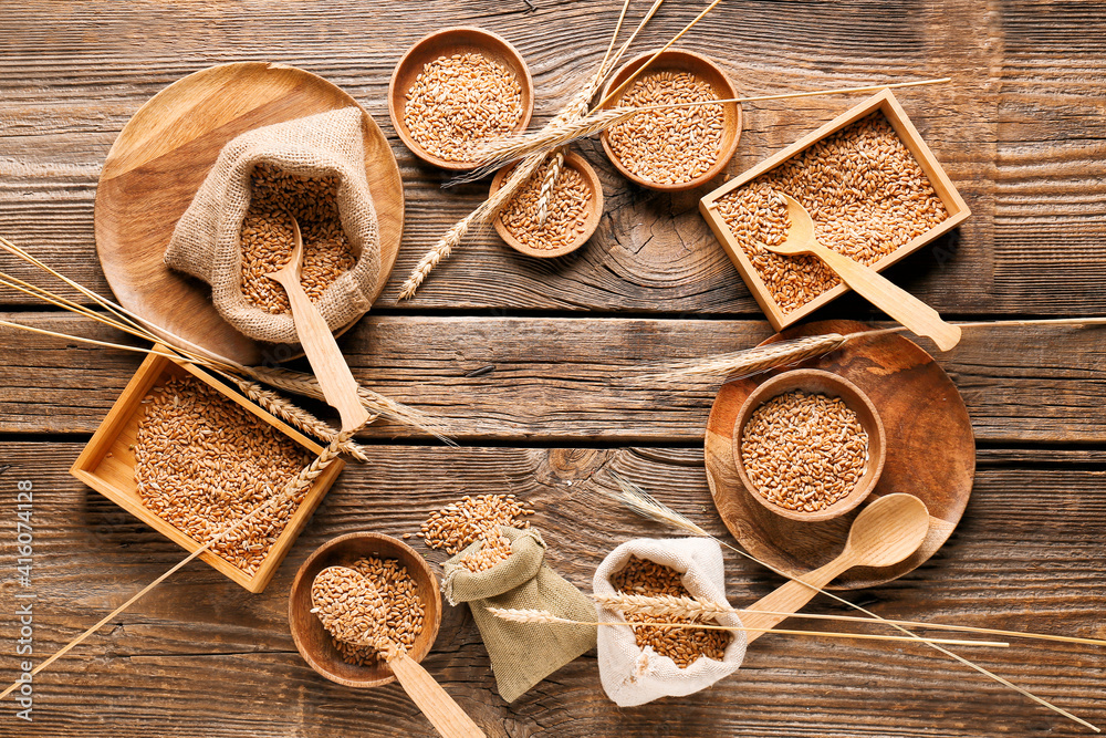 Frame made of bowls and bags with wheat grains on wooden background