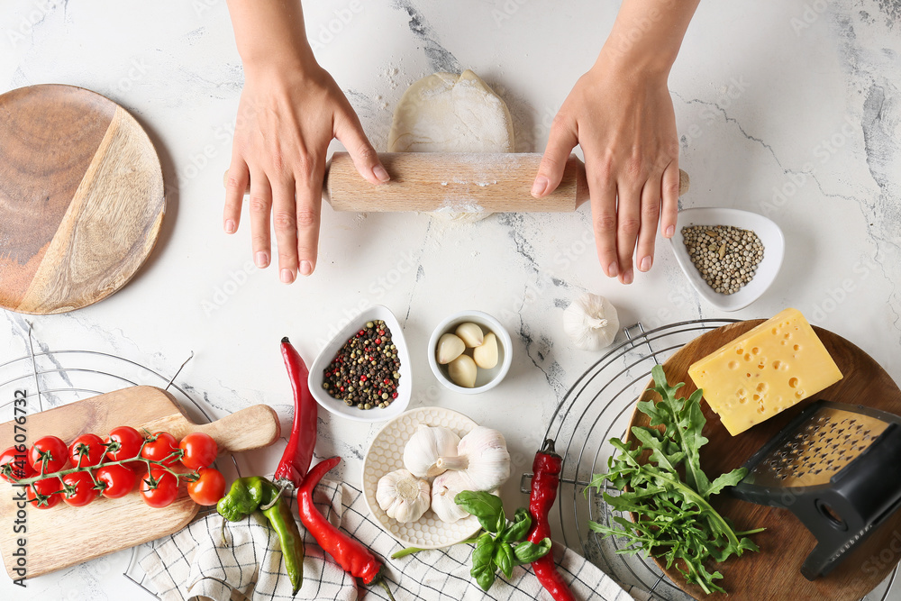 Woman making dough for pizza on light background