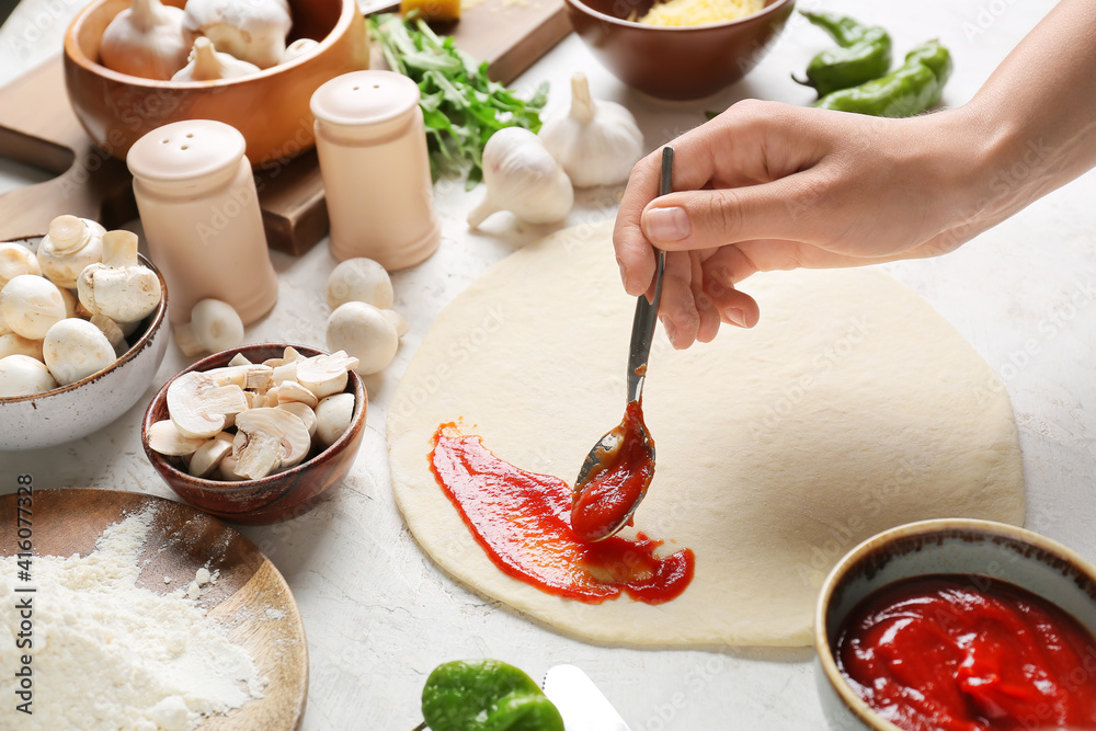 Woman making pizza on light background