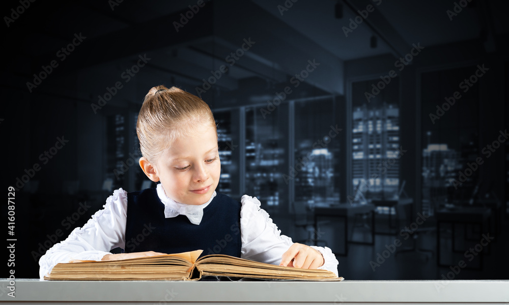 Smiling little girl sitting at desk with open book