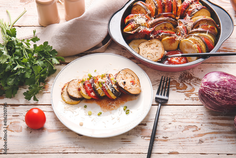 Tasty baked eggplant and tomatoes on light wooden background