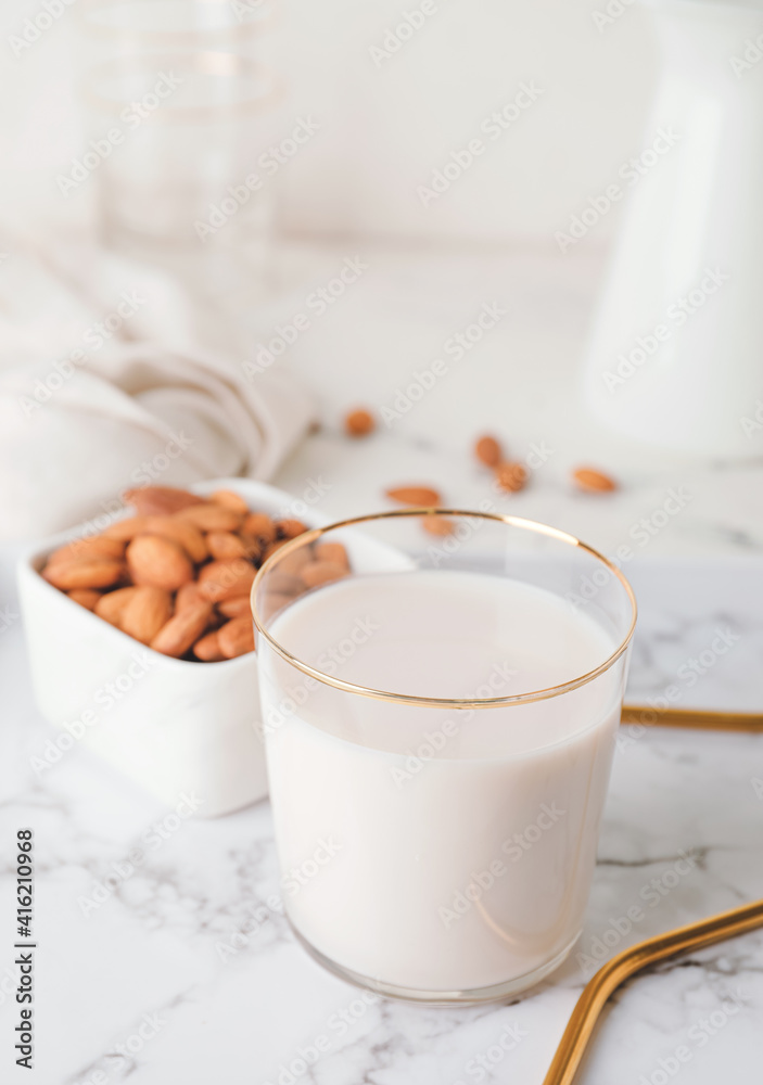 Glass of tasty almond milk and bowl with nuts on light background