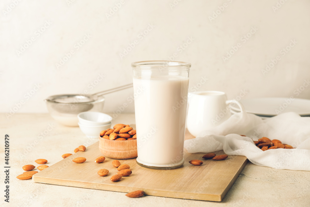 Glass of tasty almond milk on light background