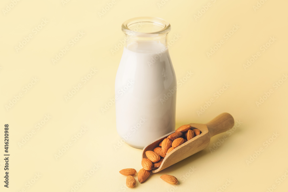 Bottle of tasty almond milk and scoop with nuts on color background