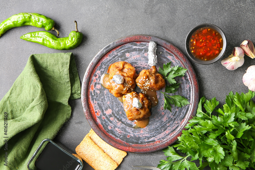 Plate with tasty chicken lollipops on dark background