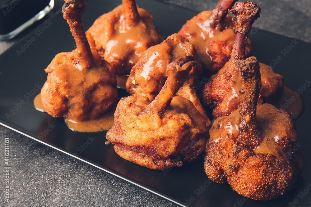 Plate with tasty chicken lollipops on dark background