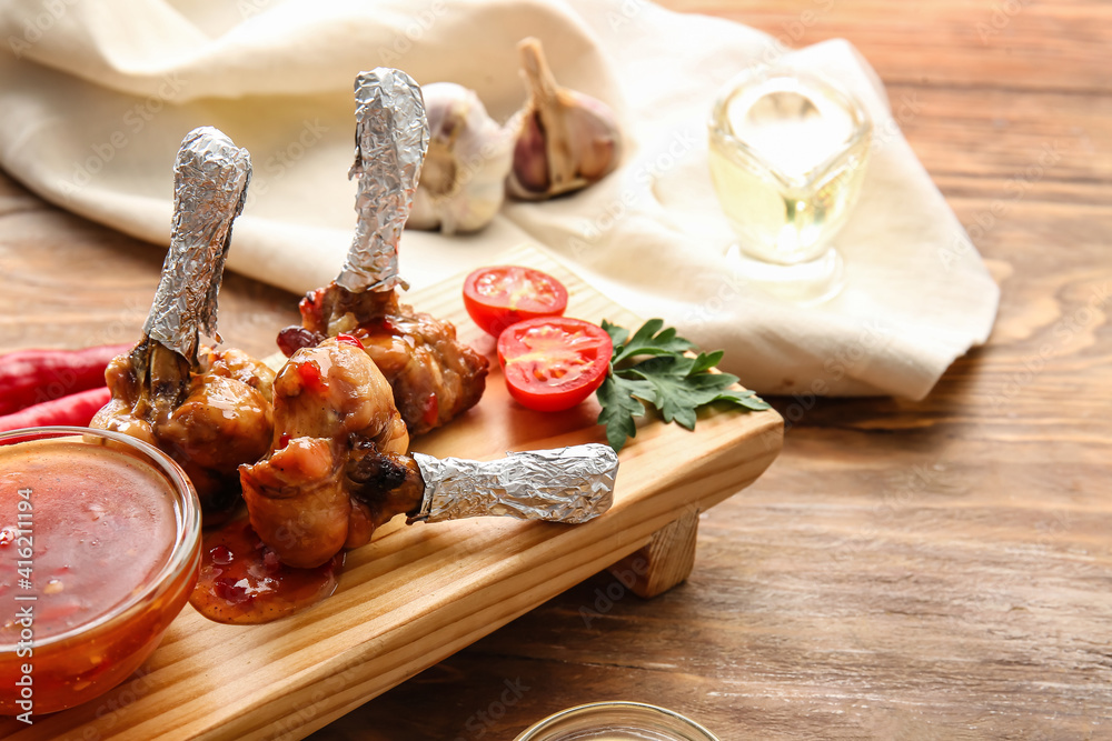 Board with tasty chicken lollipops and sauce on wooden background