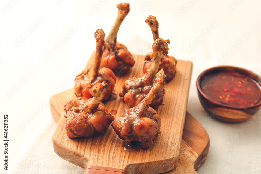 Board with tasty chicken lollipops and sauce on light wooden background