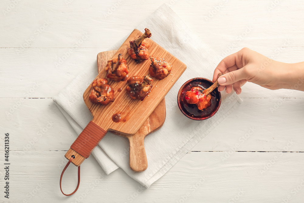 Woman eating tasty chicken lollipops  with sauce on light wooden background