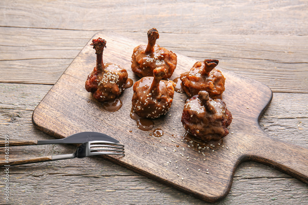 Board with tasty chicken lollipops on wooden background