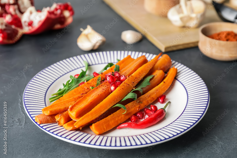 Plate of tasty baked carrot on dark background