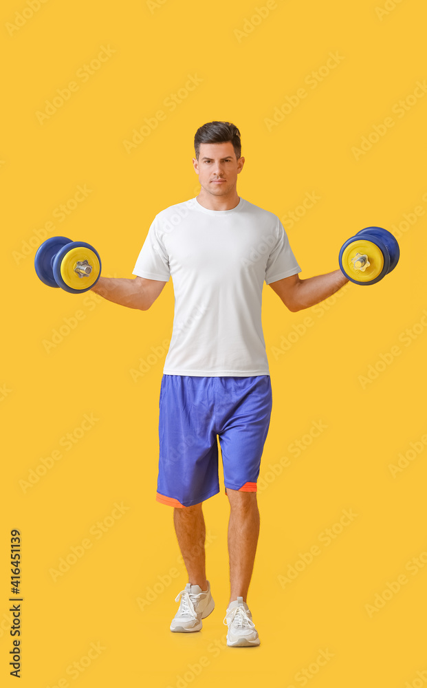 Sporty young man training with dumbbells on color background