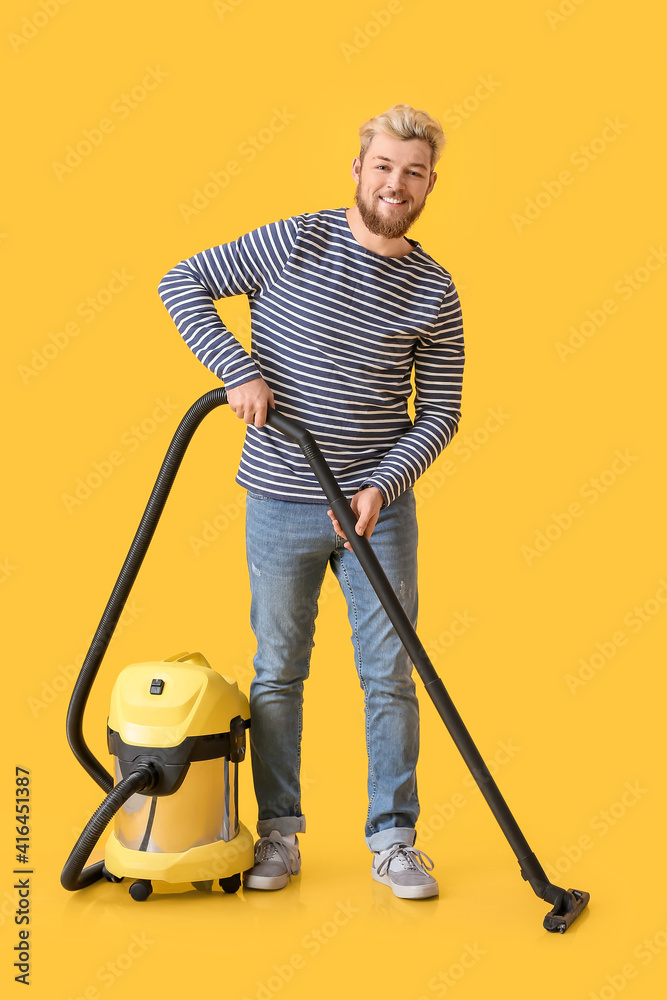 Young man with vacuum cleaner on color background