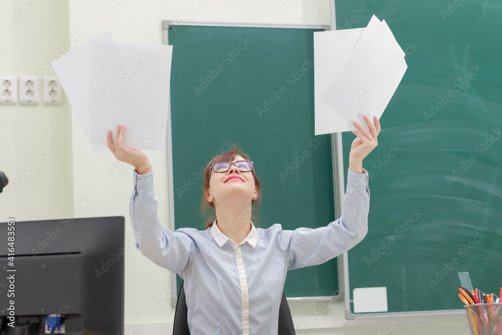 cute young woman teacher at school at her workplace sitting at the table holding documents in her ha