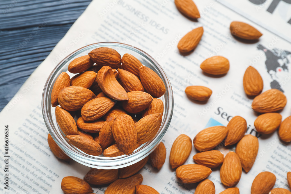 Bowl of healthy almonds and newspaper on color wooden background