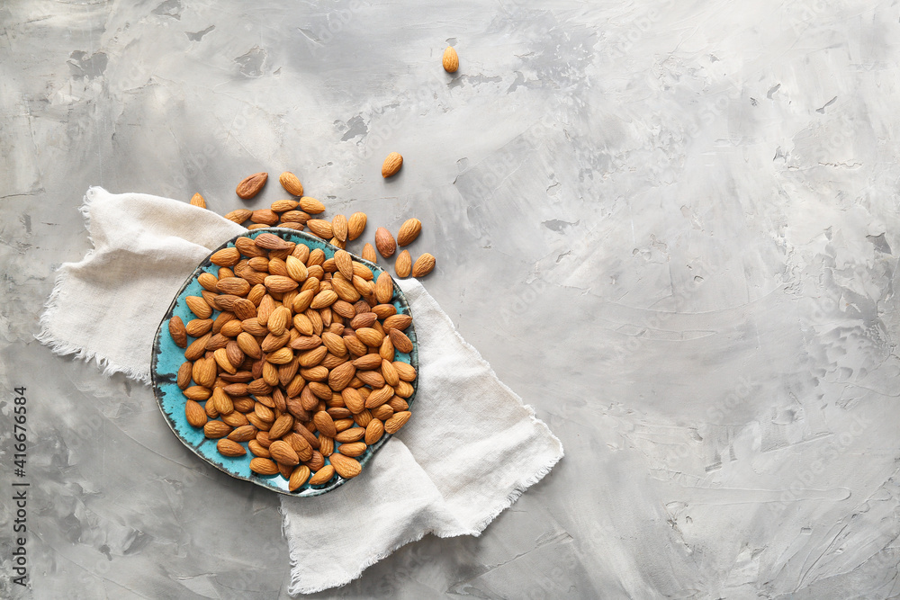 Plate with tasty almonds on grey background