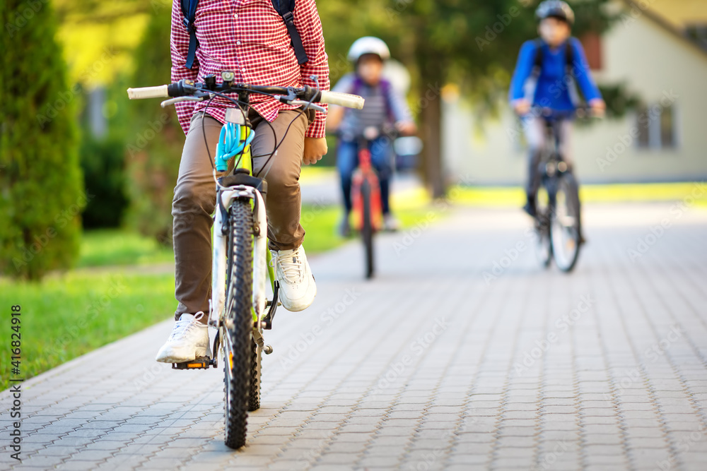 Children with rucksacks riding on the bikes in the park near the school