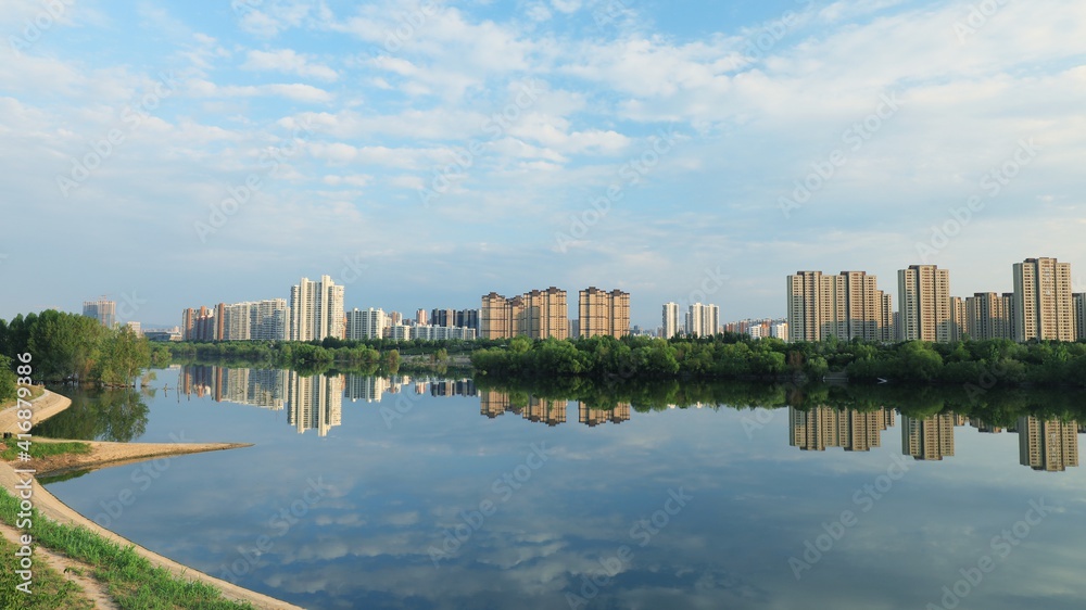 城市建筑和云朵在平静的公园湖面上的倒影