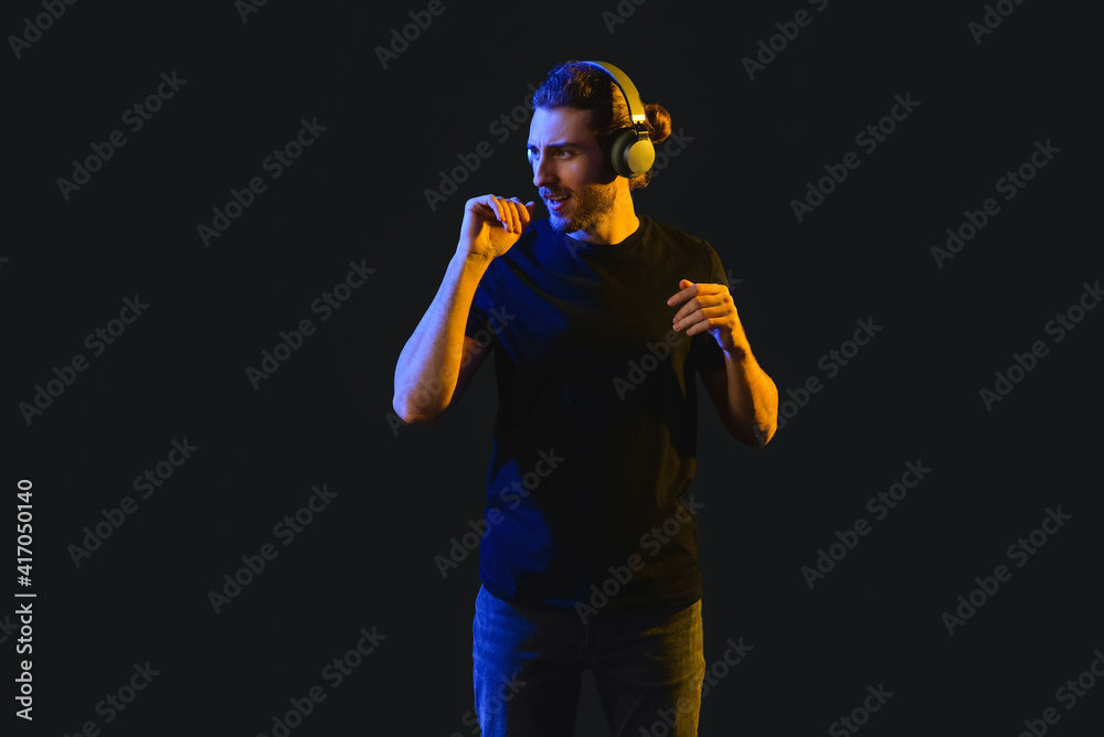 Handsome young man listening to music on dark background